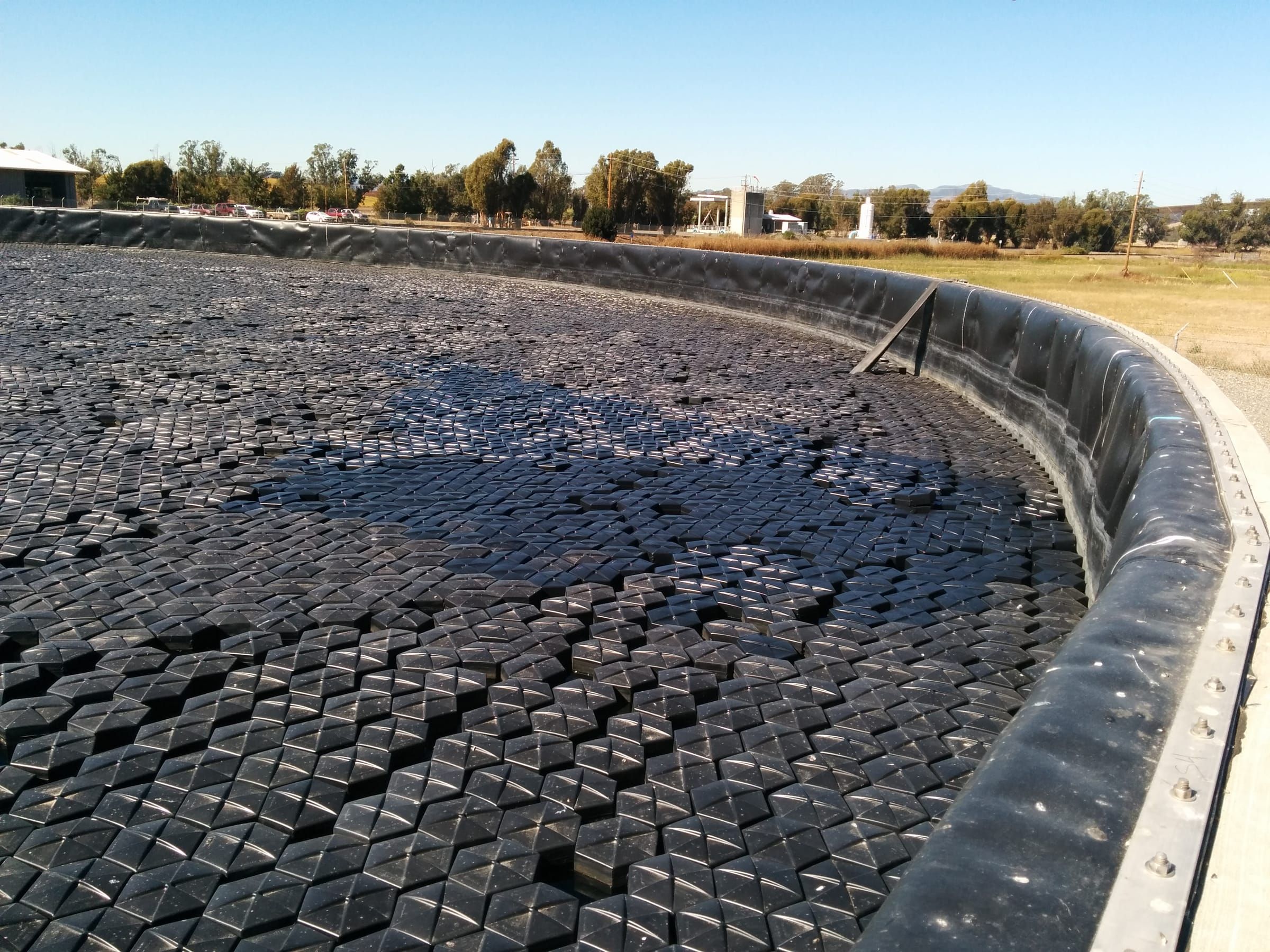 Hexprotect SLIM low-profile patent-protected floating cover installed on a wastewater treatment lagoon, providing wind-resistant surface coverage with reduced material profile