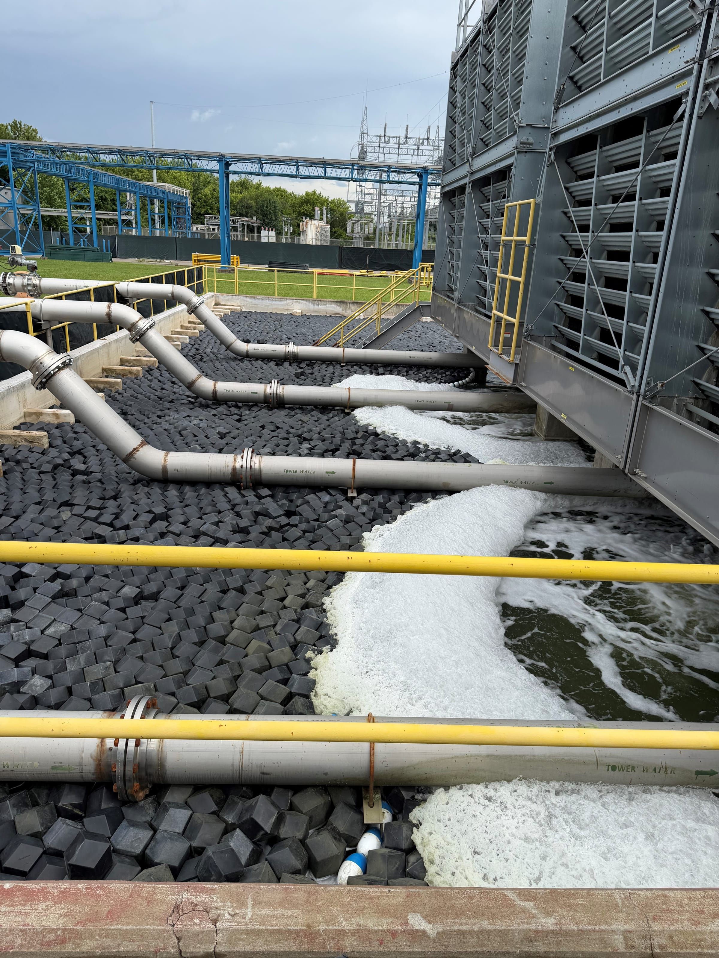 Industrial cooling tower with tower-water pipes and an open cold-water basin — the open water bodies around the cooling system that AWTT covers protect