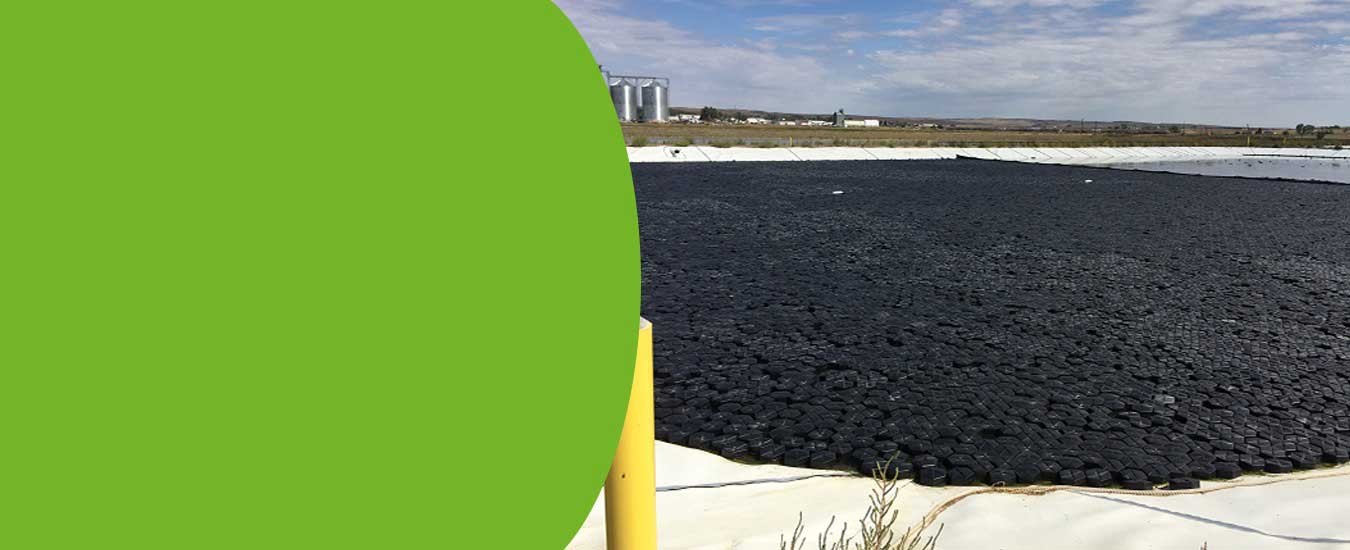 Hexprotect AQUA wind-resistant interlocking hexagonal HDPE floating covers deployed across a large outdoor industrial pond providing 99% surface coverage with 130 MPH wind resistance