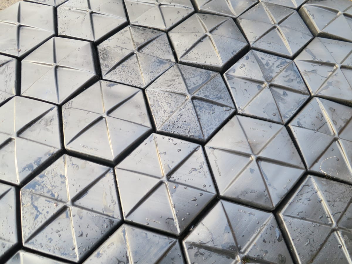 Close-up view of interlocking AWTT Hexprotect AQUA hexagonal tiles on a water surface, showing the pre-loaded chamber geometry