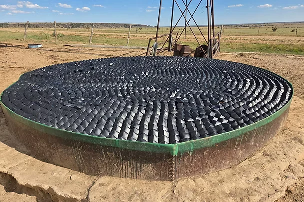 Modular floating cover installed on a windmill-fed ranch stock tank, covering the full water surface to stop evaporation