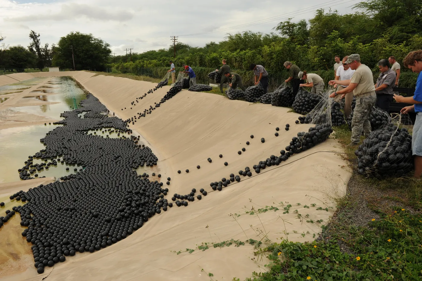 Crew installing Armor Ball floating ball covers across a lined industrial containment pond