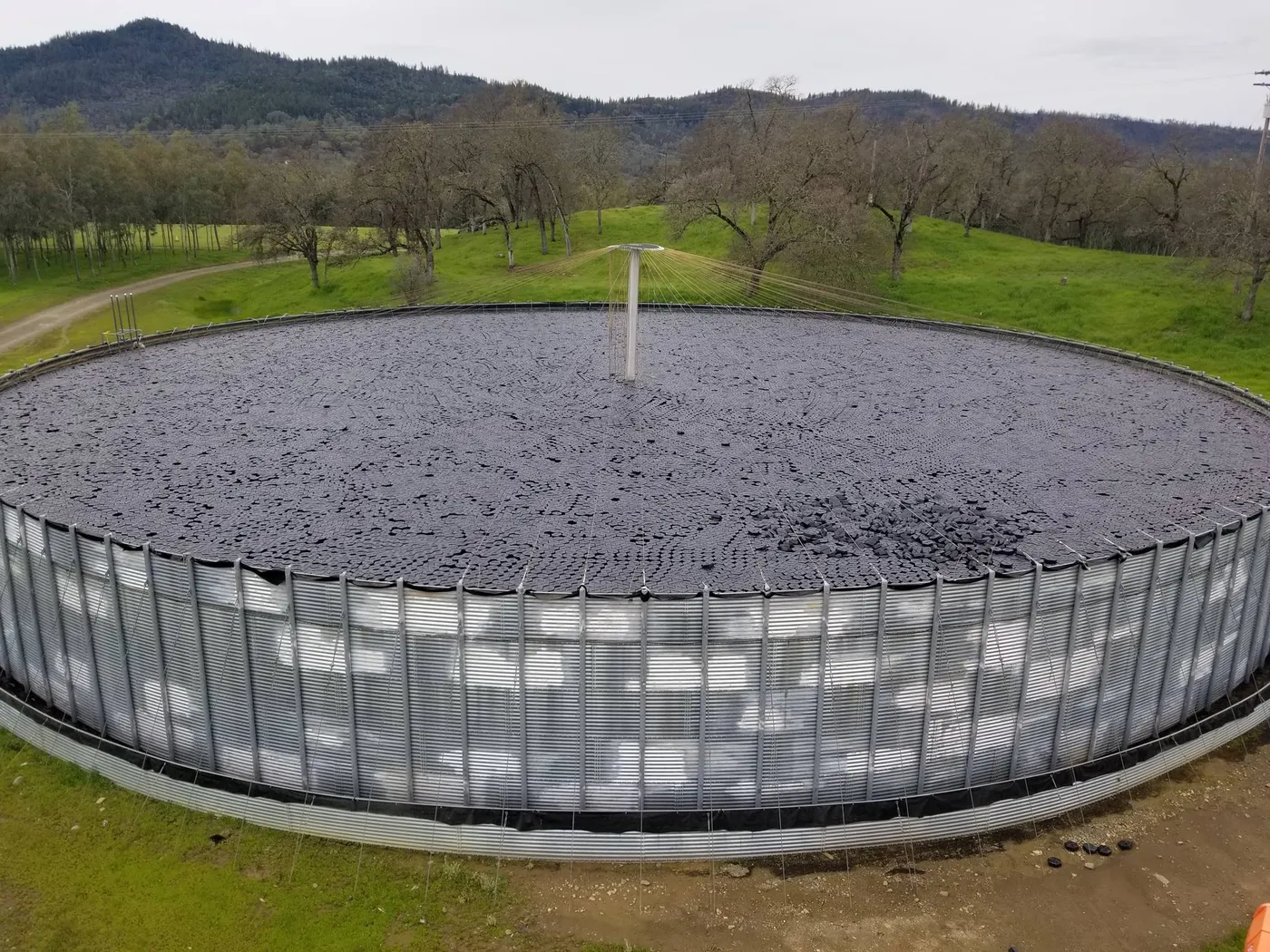 Aerial view of a round storage tank fully covered by Hexprotect AQUA floating hexagon tiles